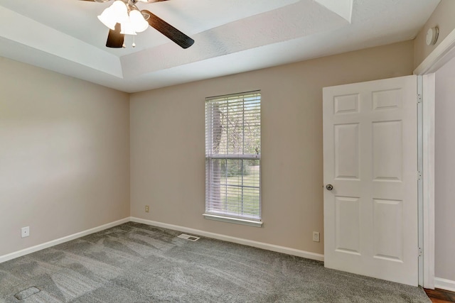 carpeted spare room featuring visible vents, a ceiling fan, baseboards, and a tray ceiling