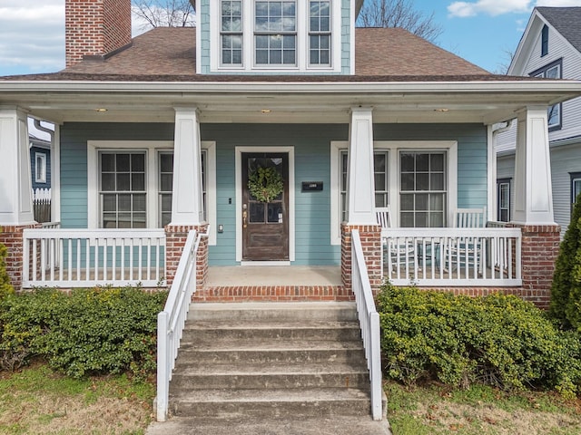 entrance to property with a porch, a chimney, and roof with shingles