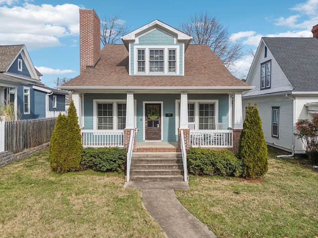 bungalow-style house featuring covered porch, fence, a chimney, and a front yard
