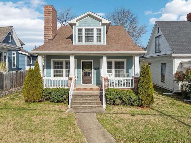 bungalow-style home with covered porch, fence, a chimney, and a front lawn