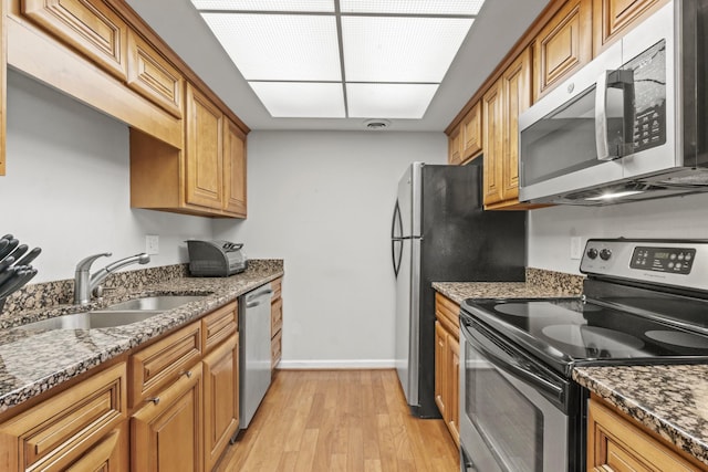 kitchen featuring light wood-style floors, baseboards, dark stone counters, a sink, and stainless steel appliances