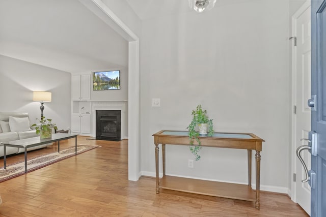 foyer featuring baseboards, a fireplace with flush hearth, and light wood finished floors