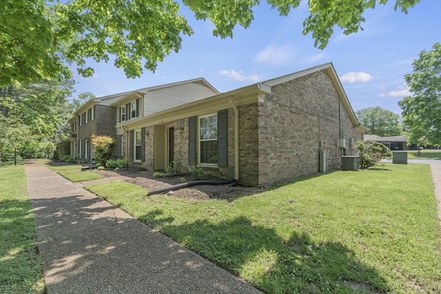 view of front facade featuring cooling unit, brick siding, and a front yard