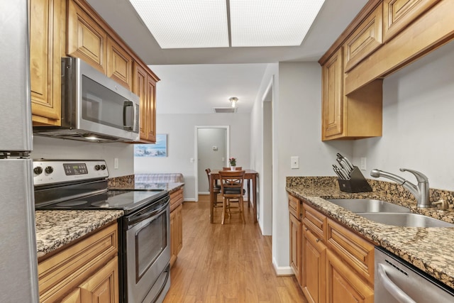 kitchen with visible vents, light stone counters, a sink, light wood-style flooring, and stainless steel appliances