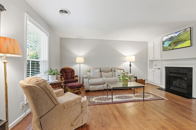 living area featuring a fireplace with flush hearth, baseboards, light wood-type flooring, and visible vents