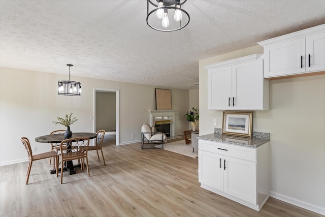 dining area featuring a notable chandelier, a fireplace, a textured ceiling, baseboards, and light wood-type flooring