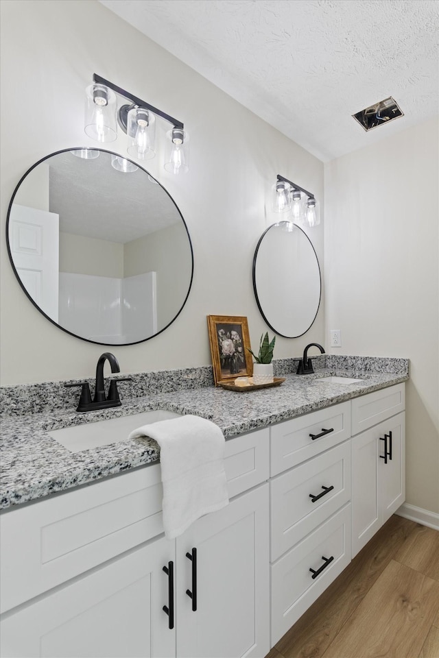 bathroom featuring double vanity, a sink, a textured ceiling, and wood finished floors