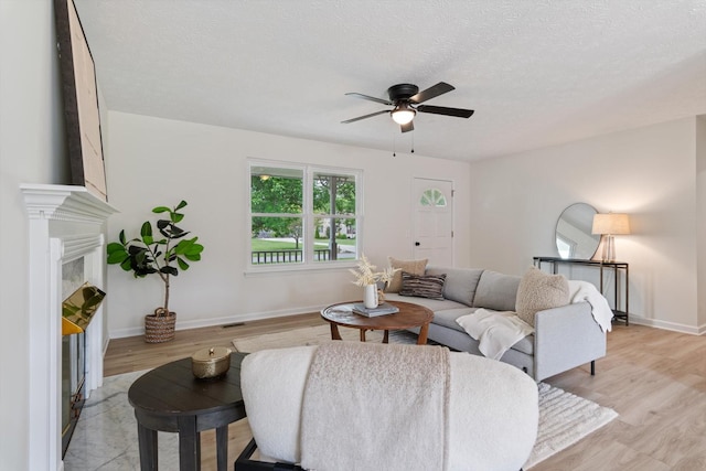 living area with a textured ceiling, ceiling fan, baseboards, and light wood finished floors