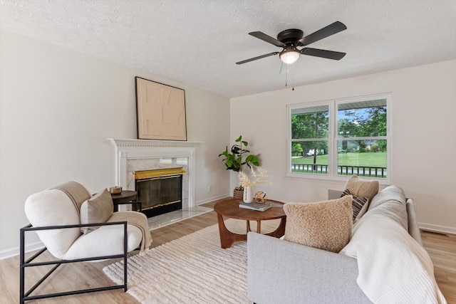 living room featuring a premium fireplace, a textured ceiling, ceiling fan, and light wood finished floors