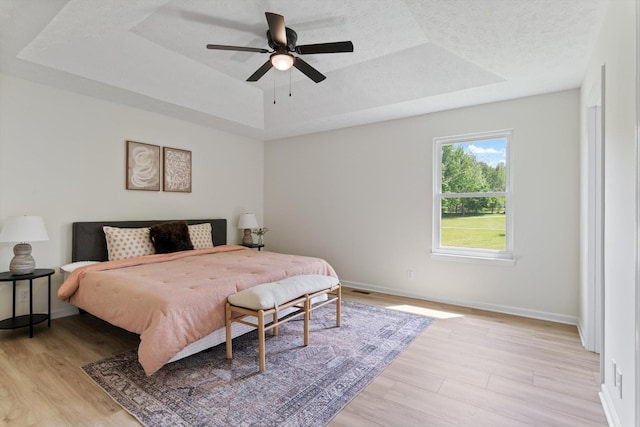 bedroom with light wood-style floors, a ceiling fan, baseboards, and a tray ceiling