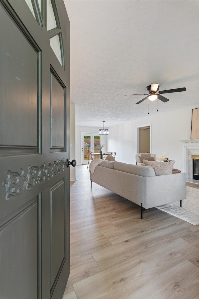 living room featuring light wood finished floors, ceiling fan with notable chandelier, and a premium fireplace