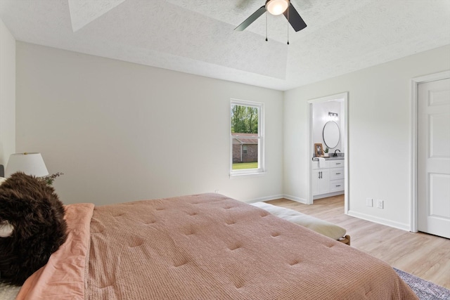 bedroom featuring a ceiling fan, a textured ceiling, baseboards, light wood finished floors, and ensuite bathroom