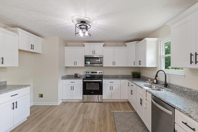 kitchen with light stone countertops, white cabinetry, a sink, stainless steel appliances, and light wood-style flooring