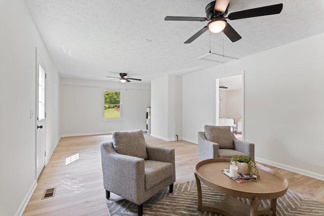 sitting room featuring ceiling fan, light wood-style floors, a textured ceiling, attic access, and visible vents
