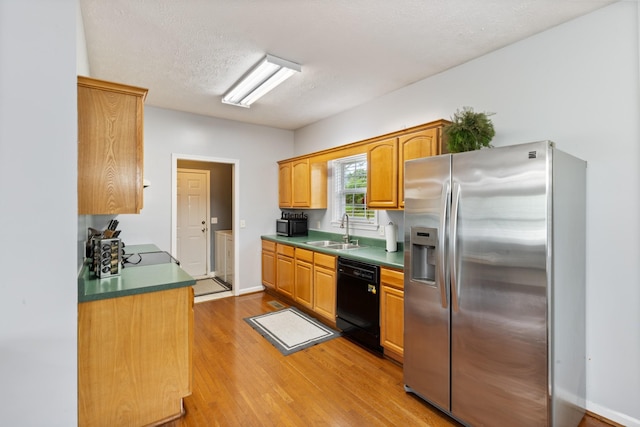 kitchen featuring light wood-style floors, baseboards, a textured ceiling, a sink, and black appliances
