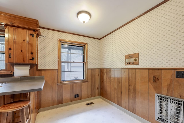 unfurnished dining area featuring visible vents, tile patterned floors, a wainscoted wall, wooden walls, and ornamental molding