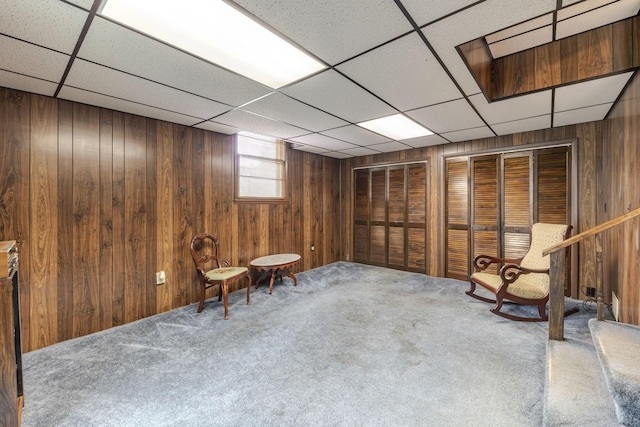 sitting room with wooden walls, a paneled ceiling, and carpet