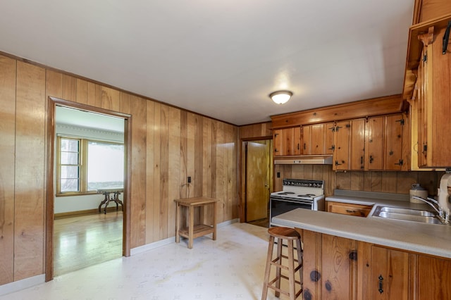 kitchen featuring brown cabinetry, wood walls, under cabinet range hood, a sink, and white electric stove