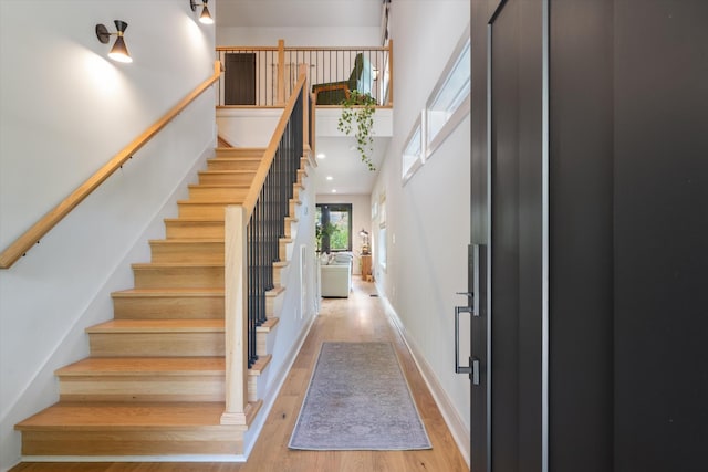 stairs with baseboards, wood finished floors, and a towering ceiling