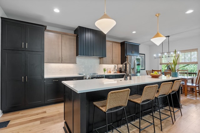 kitchen with visible vents, an island with sink, light wood-type flooring, wall chimney exhaust hood, and a sink