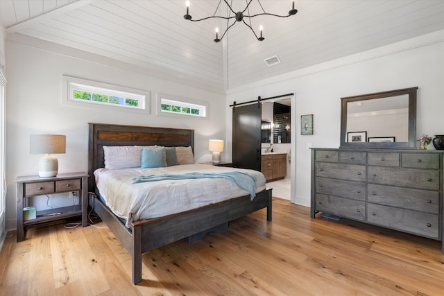 bedroom featuring visible vents, a barn door, a notable chandelier, ensuite bath, and light wood-style flooring