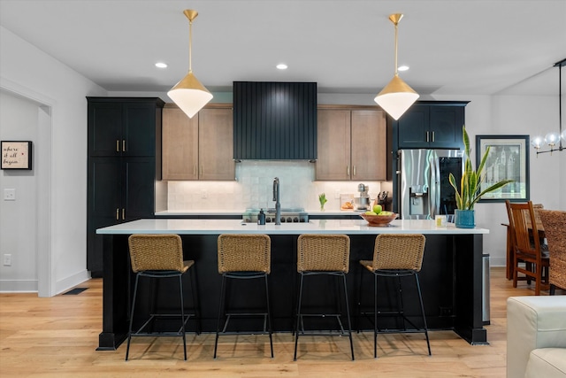 kitchen featuring tasteful backsplash, light countertops, stainless steel fridge with ice dispenser, a sink, and an island with sink