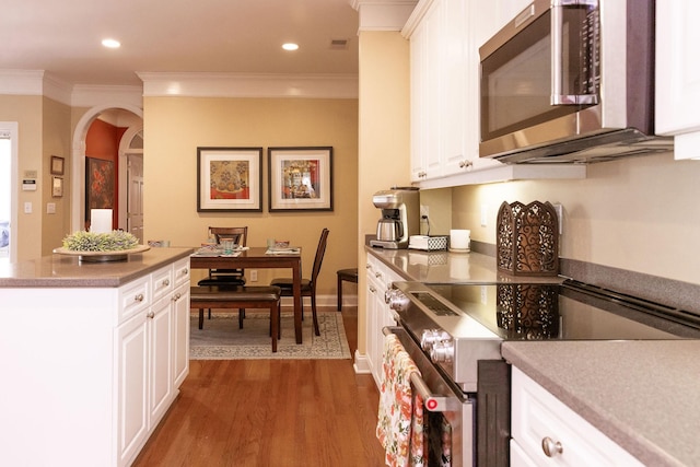 kitchen featuring white cabinets, arched walkways, stainless steel appliances, wood finished floors, and ornamental molding