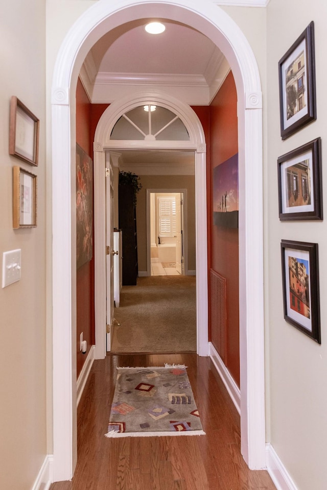 hall with crown molding, arched walkways, baseboards, and wood finished floors