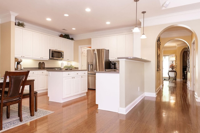 kitchen with dark countertops, appliances with stainless steel finishes, arched walkways, white cabinetry, and ornamental molding