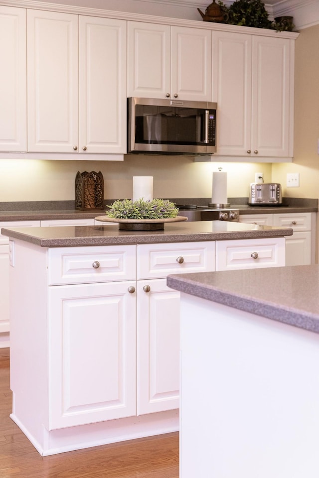 kitchen with white cabinets, stainless steel microwave, and light wood-style flooring