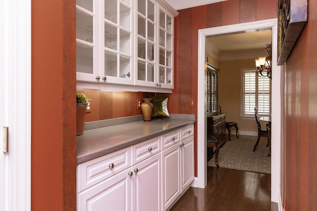 bar featuring crown molding, baseboards, dark wood-style floors, and a notable chandelier