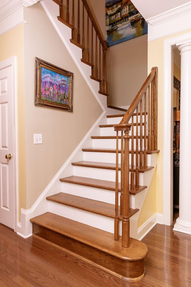 staircase with baseboards, ornate columns, and wood finished floors