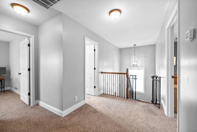 hall featuring carpet floors, baseboards, visible vents, and an upstairs landing