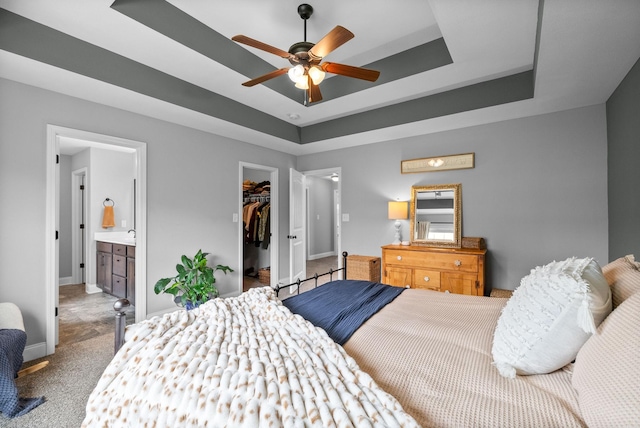 carpeted bedroom featuring a tray ceiling, a spacious closet, baseboards, and ensuite bath