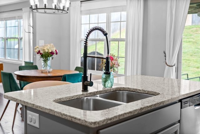 details with pendant lighting, dishwasher, a sink, light stone counters, and a notable chandelier