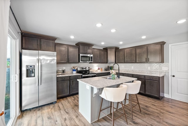 kitchen with dark brown cabinetry, a sink, stainless steel appliances, decorative backsplash, and light wood-type flooring