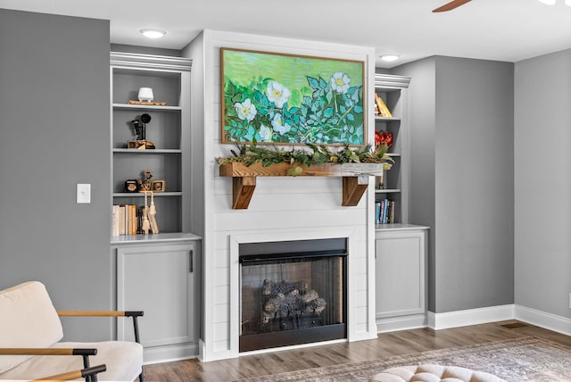 living area featuring a ceiling fan, baseboards, wood finished floors, and a fireplace