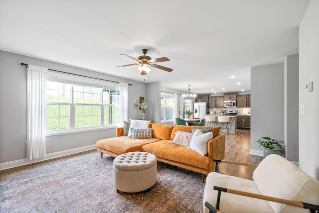 living room featuring baseboards, a wealth of natural light, ceiling fan with notable chandelier, and wood finished floors