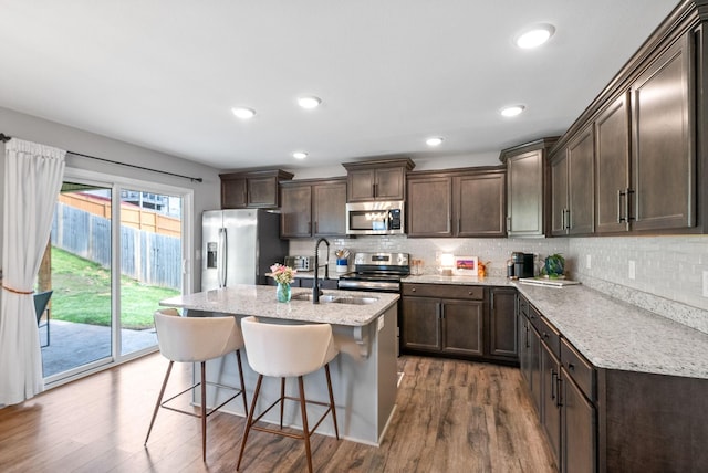 kitchen with dark brown cabinetry, a kitchen breakfast bar, dark wood finished floors, stainless steel appliances, and tasteful backsplash