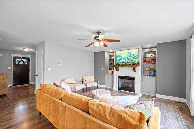 living room featuring a fireplace, built in shelves, a ceiling fan, baseboards, and wood finished floors