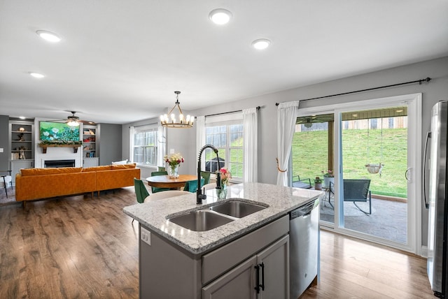 kitchen with ceiling fan with notable chandelier, a center island with sink, a sink, dark wood finished floors, and appliances with stainless steel finishes