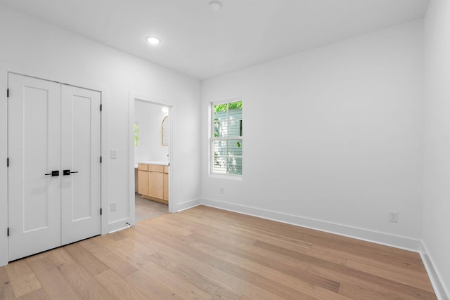 unfurnished bedroom featuring a closet, baseboards, recessed lighting, light wood finished floors, and ensuite bath