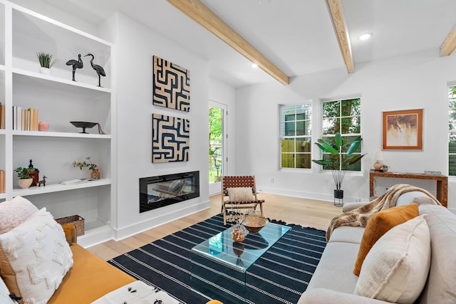 living area with baseboards, beamed ceiling, a glass covered fireplace, and wood finished floors