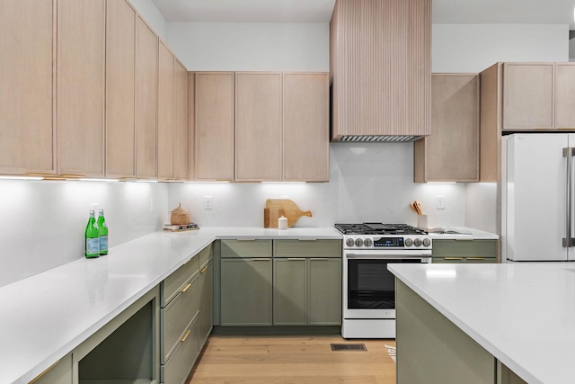 kitchen with freestanding refrigerator, light wood-style floors, stainless steel gas range oven, light countertops, and green cabinetry