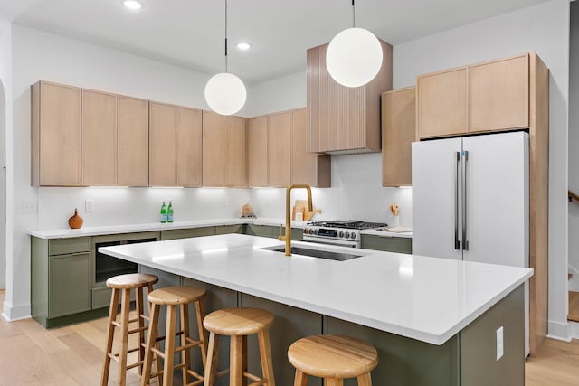 kitchen with light brown cabinets, a breakfast bar, a center island with sink, light countertops, and light wood-style flooring