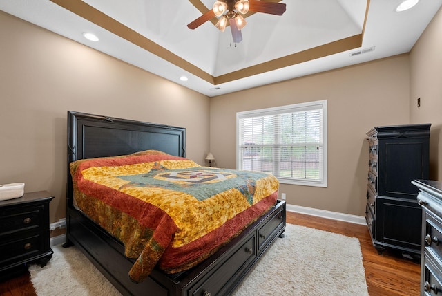bedroom featuring visible vents, wood finished floors, baseboards, a tray ceiling, and recessed lighting