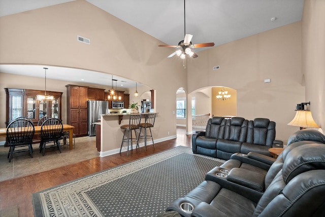 living room featuring visible vents, arched walkways, wood finished floors, high vaulted ceiling, and ceiling fan with notable chandelier