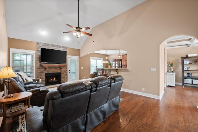 living area featuring ceiling fan, arched walkways, a brick fireplace, wood finished floors, and baseboards