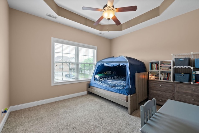 carpeted bedroom featuring a ceiling fan, baseboards, visible vents, and a tray ceiling