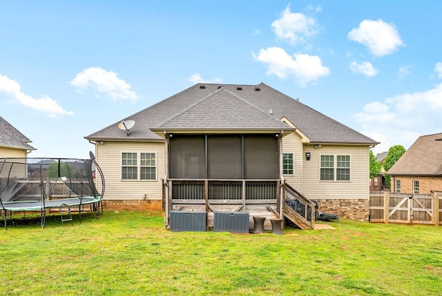 rear view of house featuring a sunroom, a trampoline, roof with shingles, and a yard